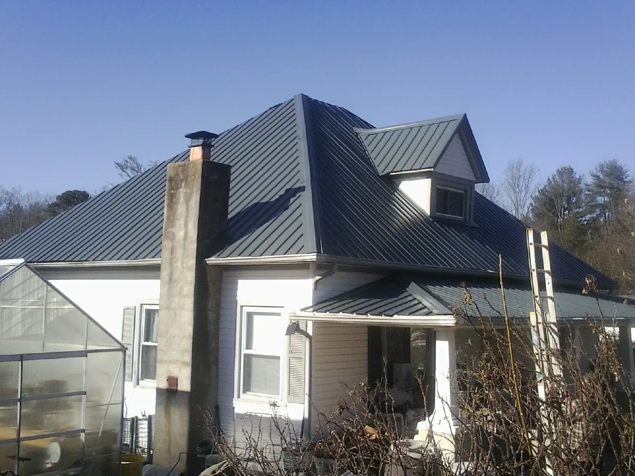Dark blue standing seam metal roof on a white farmhouse with dormer — Slate & Tile Roof Repair by Roofing Brothers in Holiday