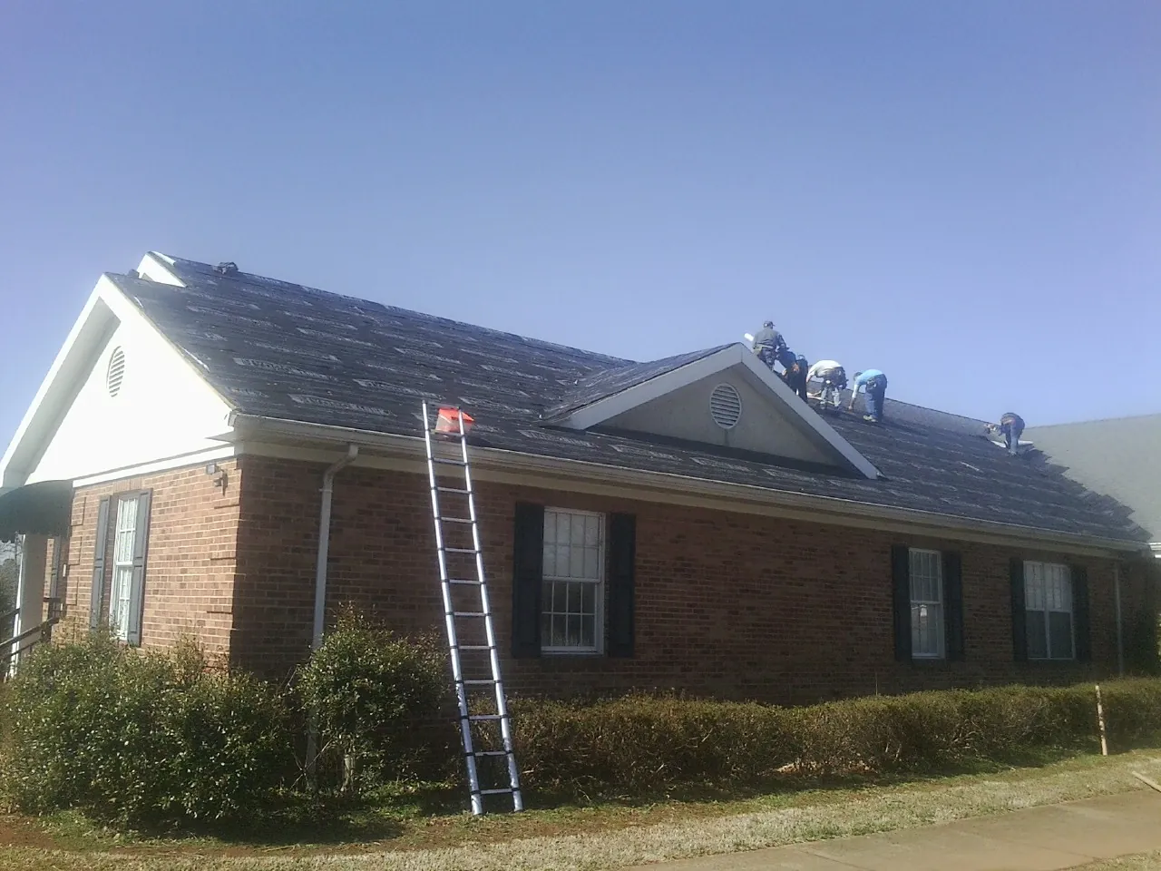 Crew tearing shingles off a brick ranch roof with a ladder set — Emergency Roof Repair work by our crew in Holiday