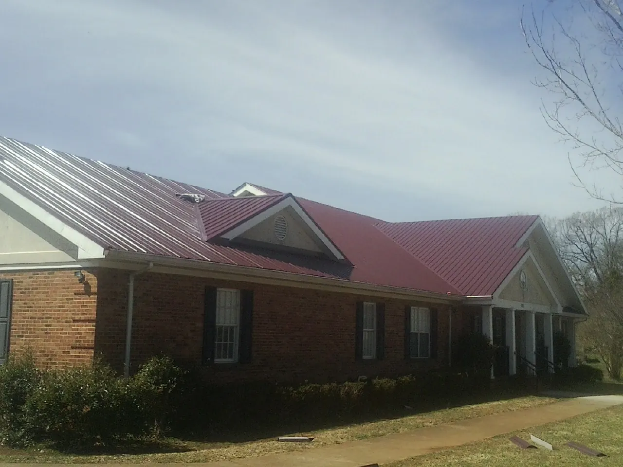 Red metal roof with gabled entries on a long brick building, from a Hail Damage Roof Repair job in Holiday