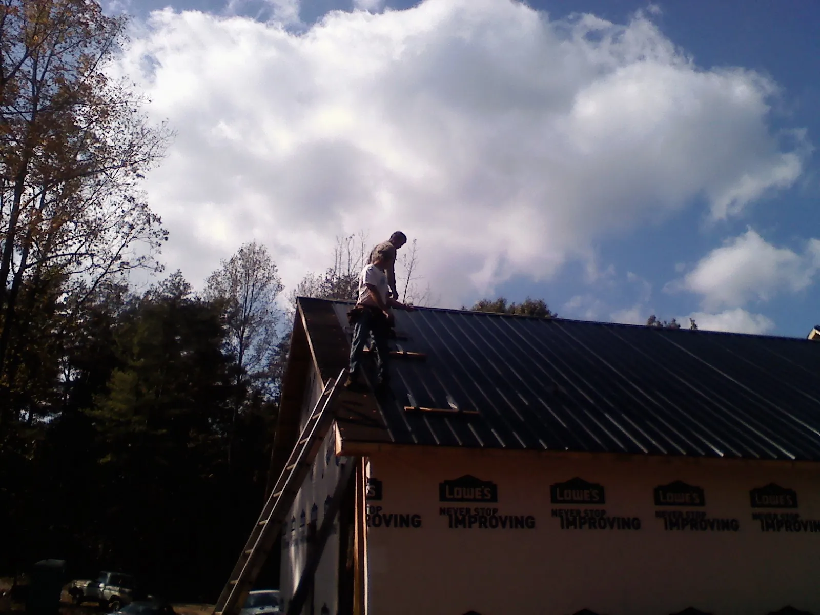 Roofer fastening dark metal panels high against a cloudy sky, from a Roof Inspection job in Holiday