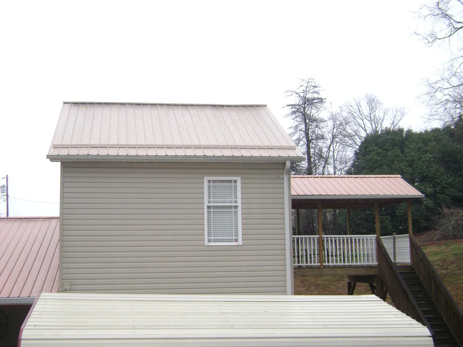 Tan metal roofs on a two story addition and attached porch, from a Roof Replacement job in Holiday